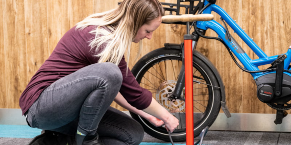 Bike maintenance workshop photo shows a person kneeling down with a bike tire pump next to a bike