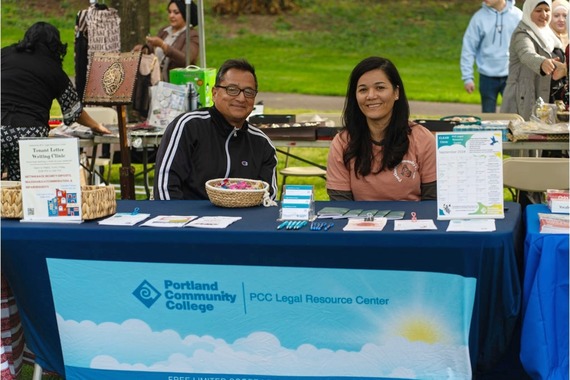 Two people smile while sitting at a table with a PCC tablecloth that says: legel service clinic