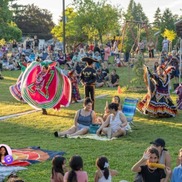 A grassy field filled with people on picnic blankets and traditional dancers in costume