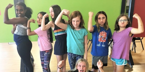 A line of children smile and flex their arms in a self defense class - Rose City Self Defense