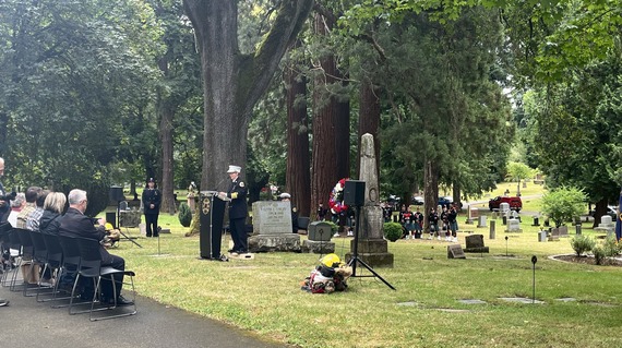 row of people in chairs watching speaker in firefighter's uniform at podium in cemetery
