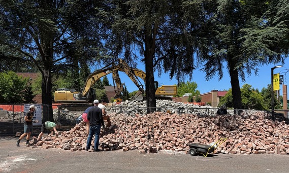 A large pile of bricks from an old building are looked over and some people are loading them up to take them away from the brick giveaway