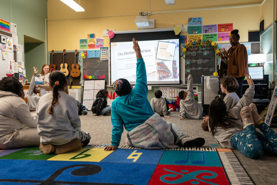 ARTS - Students on the floor of a bright classroom with one hand raised and a teacher standing - credit PDX Jazz