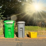 A bright sun in the sky, over a couple curbside garbage containers for early pickup on hot days - trash pickup - trash cans