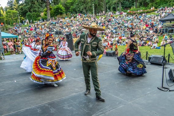 Folk dancers perform at Washington Park in front of a large audience seated on a grassy hill