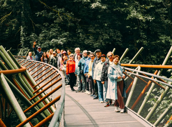 A group of smiling people pose along a pedestrian bridge near Hoyt Arboretum