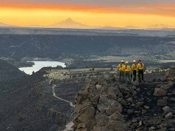 Four wildland firefighters look out from a bluff in Central Oregon with an orange sky and mountain