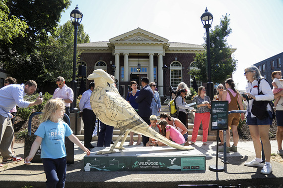 A crowd of people outside the St. Johns Library gather around a 6-foot crow sculpture