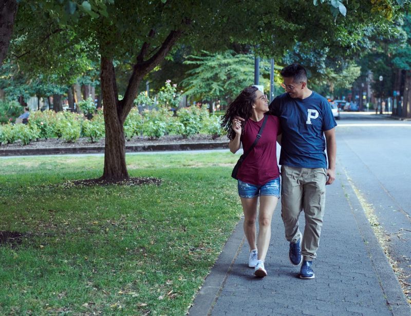 Two people walking along street under trees