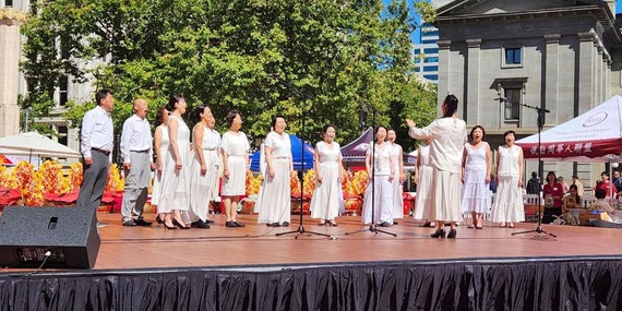 ARTS - A choir, all wearing white, singing on top of a stage in Pioneer Courthouse Square.