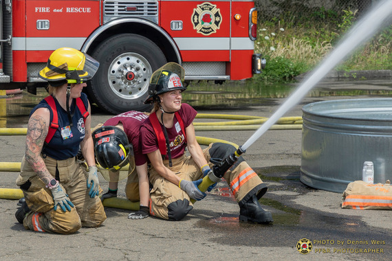 Young women work hard practicing using a fire hose with help from a firefighter