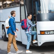 Two people board a bus, pulling luggage with them