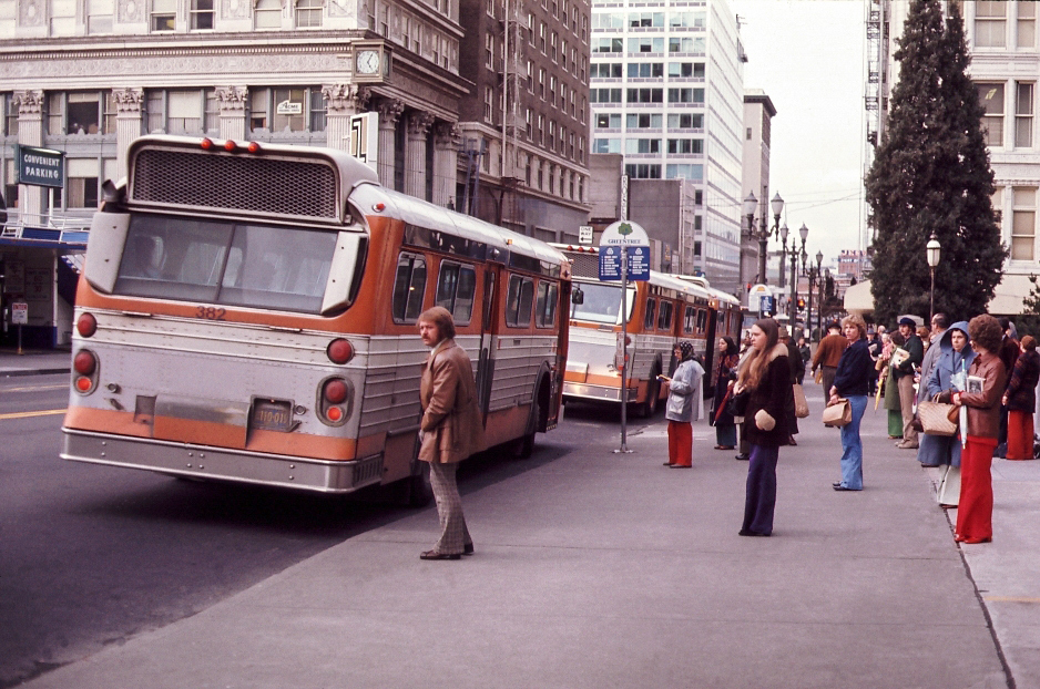 People in 70s clothing waiting for orange TriMet buses