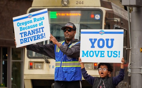 Image of a man and a child holding signs thanking transit drivers.