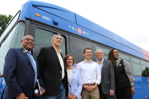Secretary of Transportation Pete Buttigieg poses in front of a TriMet all-electric bus with others