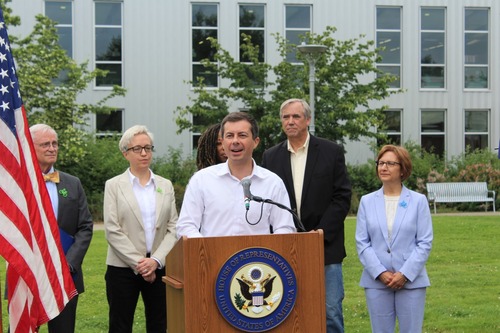 Secretary of Transportation Pete Buttigieg stands behind a podium sharing his remarks to an audience