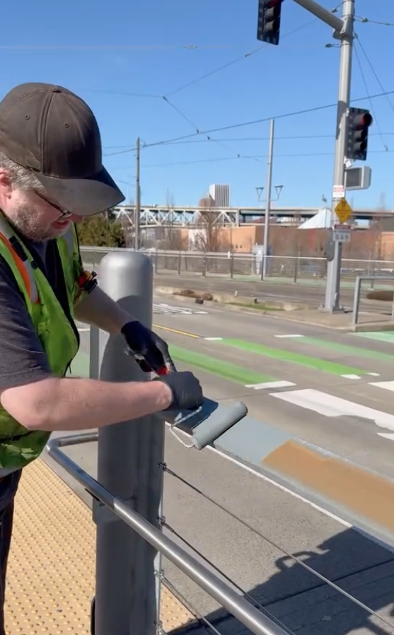A TriMet employee using a hand brush roller to paint at a station