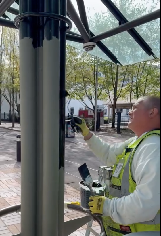 TriMet employee using a hand brush roller to paint at a station 
