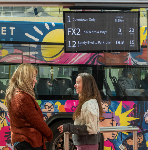 Two riders standing in front of a digital display showing arrival times
