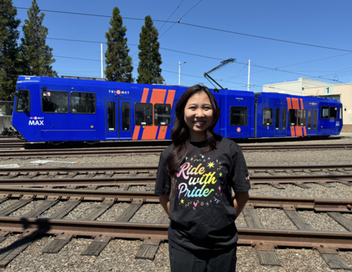 Woman wearing a Pride t-shirt in front of a train at a TriMet facility