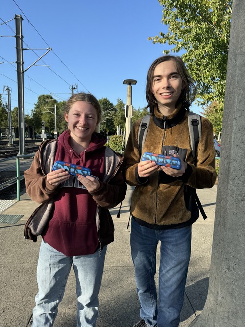 Two riders holding up squishy trains at a MAX station