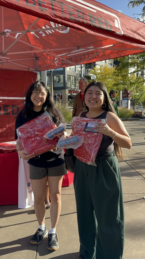 Two riders holding up squishy trains and Better Red bags at a MAX station