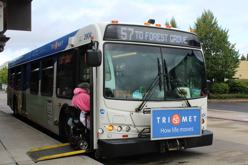 This is a photo of a person in a mobility device using a ramp to board TriMet Line 57 at a transit center.