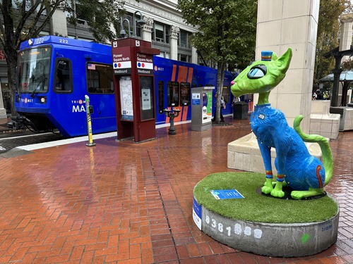 A sculpture of a cat in Downtown Portland next to a MAX train