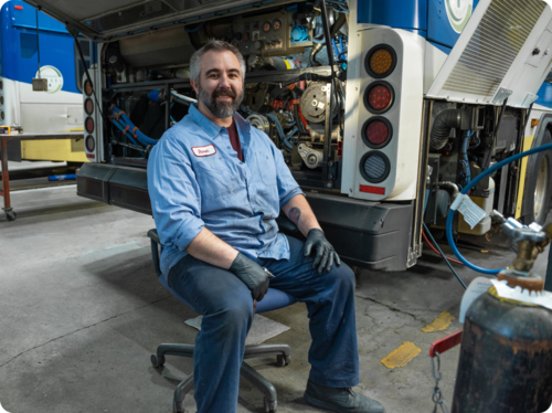 Mechanic at TriMet garage sitting next to a bus