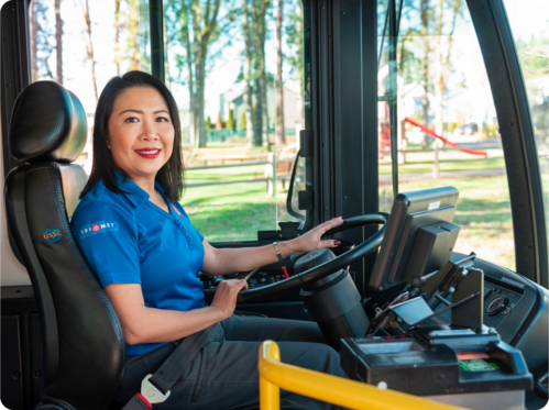 Bus driver holding steering wheel and facing camera