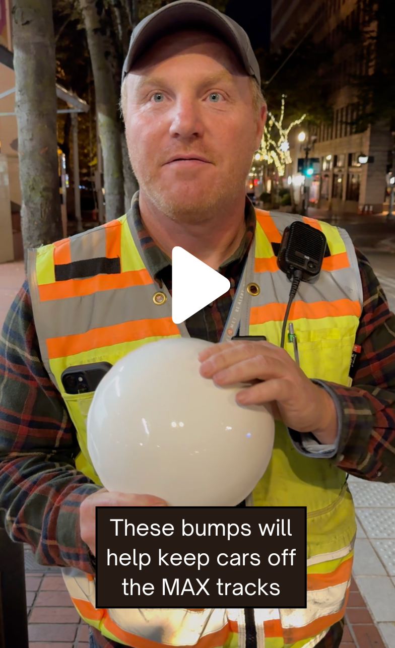 Maintenance team member holding up a white traffic button next to the MAX tracks at night