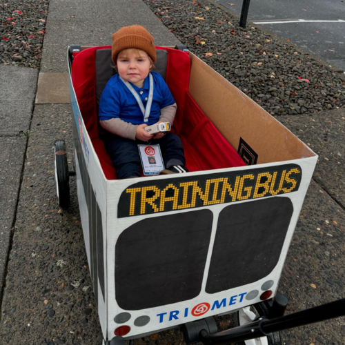 Toddler in a TriMet uniform riding in a bus decorated wagon