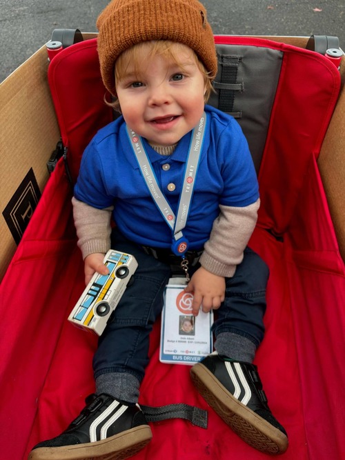 Toddler in a TriMet uniform riding in a bus decorated wagon