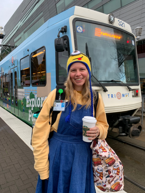 Woman wearing a "Stuart the Minion" beanie next to a MAX train