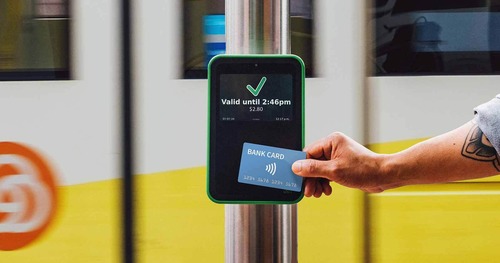 Image of a person tapping a bank card at a green Hop reader with a MAX train in the background.