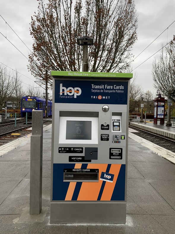 This photo shows a TriMet fare vending machine at the Beaverton Transit Center MAX platform. A MAX train is in the background.