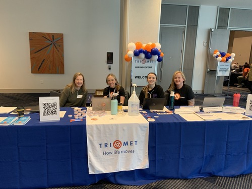 Image of four TriMet representatives seated behind a table with a sign reading "TriMet Hiring Event"