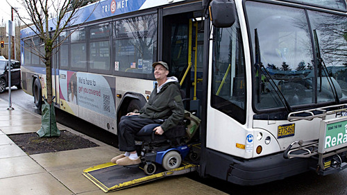 Image of Bill, a TriMet rider, exiting a bus down the front ramp on his motorized wheelchair