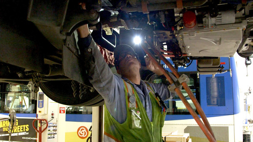 Image of a mechanic wearing safety equipment and working underneath a bus at the TriMet Powell Operations Facility