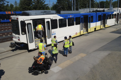 A group of people wearing high-visibility safety vests gathered around a TriMet MAX Type 1 train