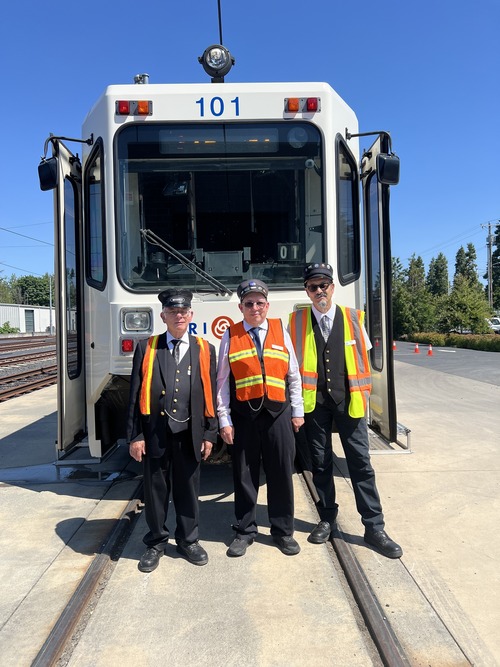 Three men dressed in formal conductor uniforms with cap in front of MAX Train 101