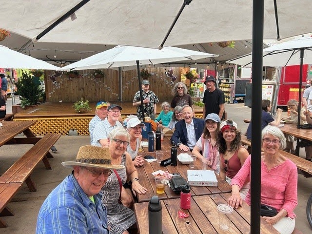 Image of people, including Portland Mayor Keith Wilson, smiling for a photo while sitting at a food cart pod