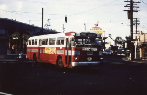 A vintage red and white bus travels along a city street