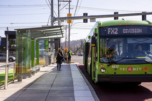 Image of a green TriMet FX2-Division bus serving a station on Southeast Division Street in Portland