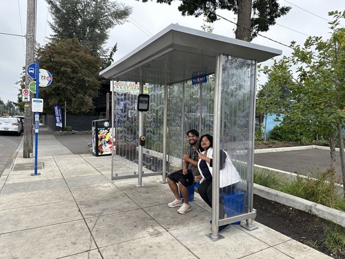 Vew of a bus stop showing two people sitting and smiling inside a bus shelter
