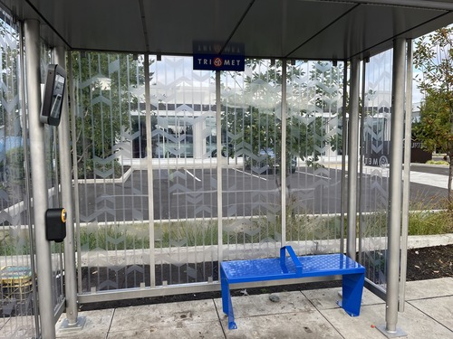 Inside the bus shelter looking toward a simple blue bench and the patterned glass walls