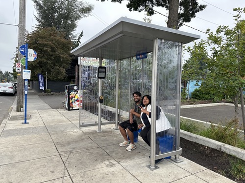 Two people pose for a picture while sitting in a next-generation TriMet bus shelter in Northeast Portland