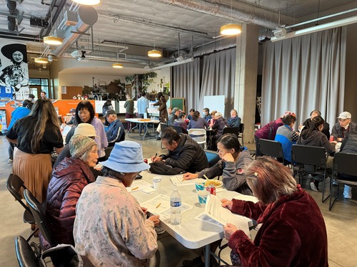 Attendees at a TriMet open house sit at a table with service maps in the background
