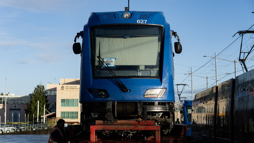 A brand-new blue MAX train car, labeled 627, is shown from the front while still secured on a red transport trailer.