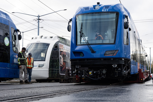 A brand-new blue MAX train car, numbered 627, is being carefully lowered onto the tracks from a transport trailer